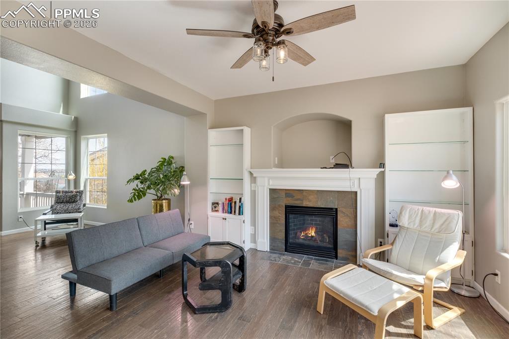 Image 9 of 39: Living area featuring wood finished floors, a ceiling fan, and a tiled fire