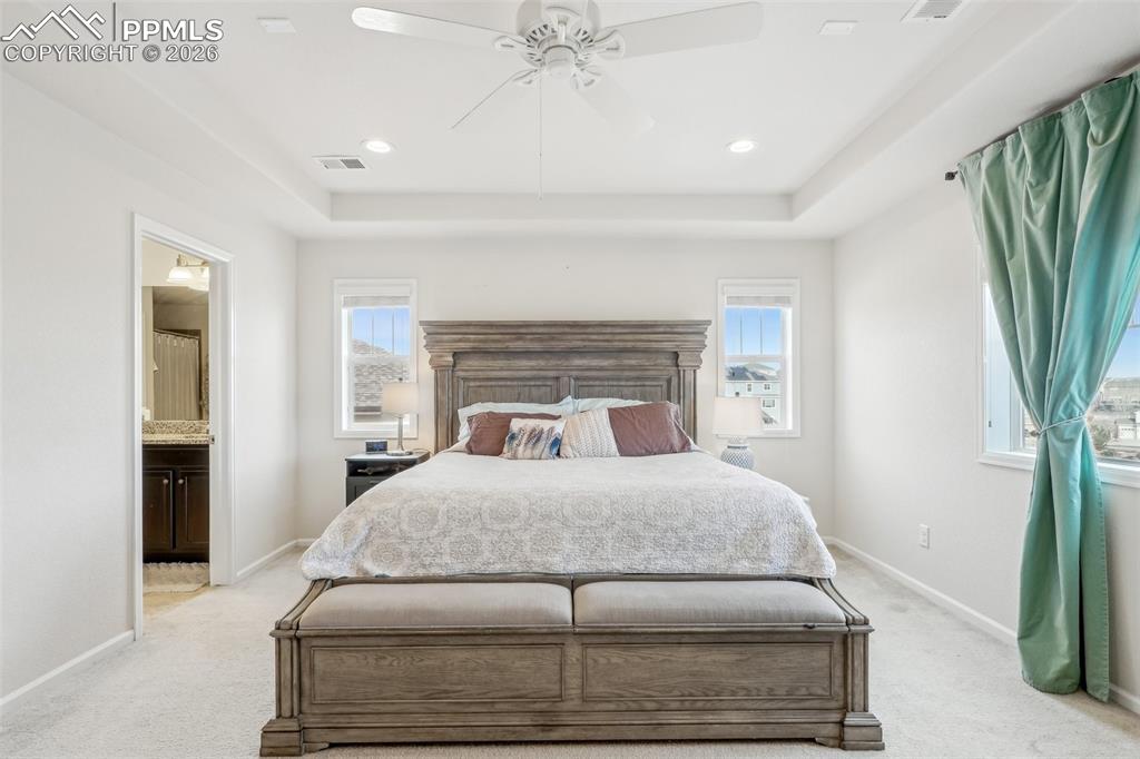 Image 25 of 50: Primary bedroom with tray ceiling, carpet, en suite bathing 