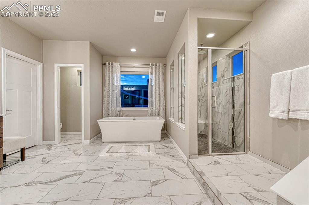 Image 20 of 48: 5 piece primary bath ensuite with marble finish floors, a soaking tub, an e