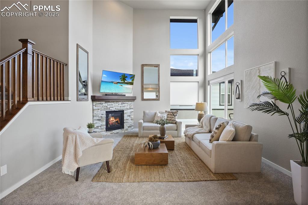 Image 12 of 50: Living area featuring a towering ceiling, a fireplace, baseboards, and carp