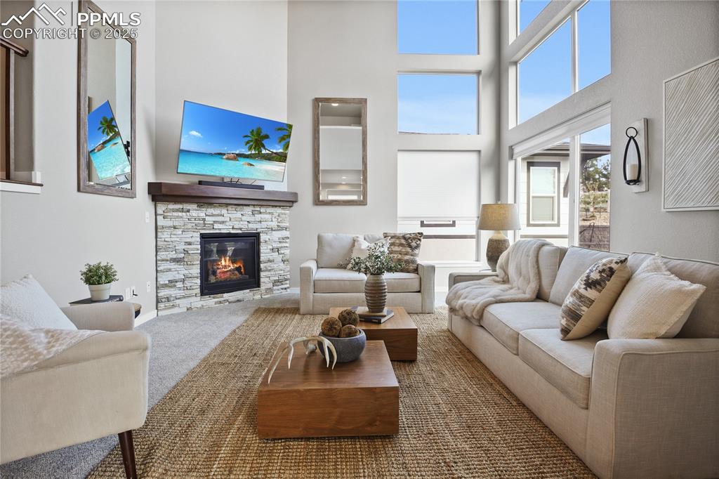 Image 13 of 50: Living room with a high ceiling, a stone fireplace, and carpet flooring
