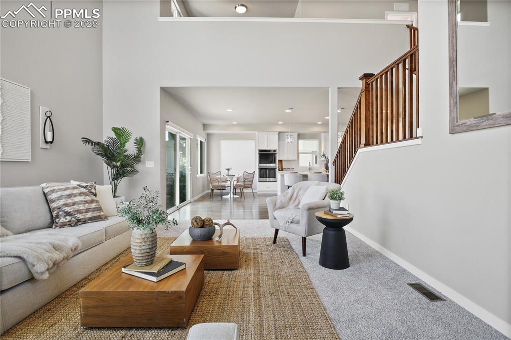 Image 16 of 50: Living room featuring stairs, baseboards, recessed lighting, a high ceiling
