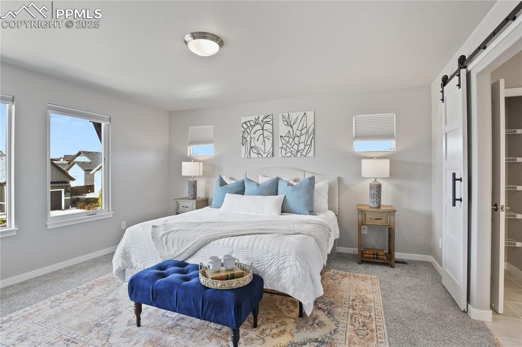 Image 27 of 50: Bedroom with a barn door, carpet flooring, and baseboards