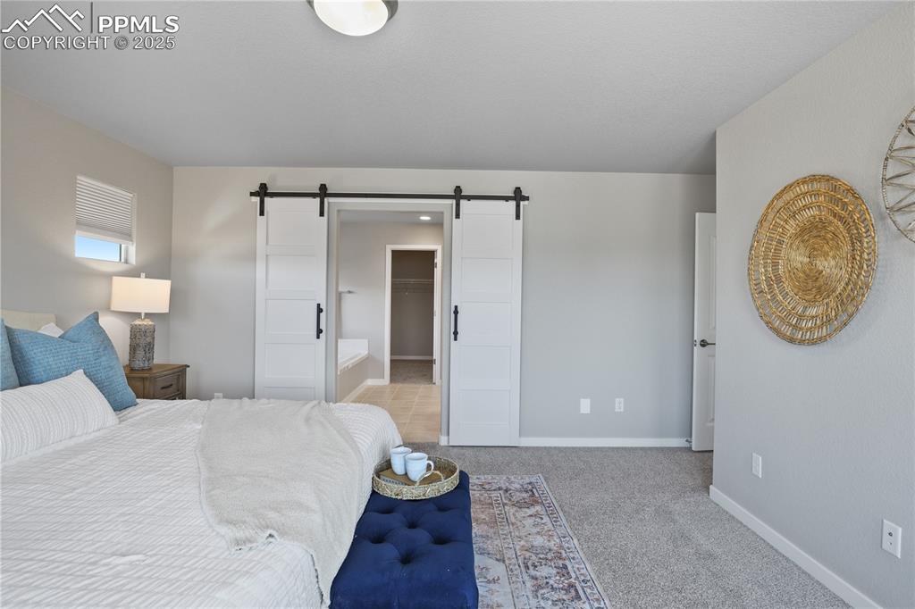 Image 29 of 50: Bedroom featuring a barn door, light carpet, baseboards, and a spacious clo