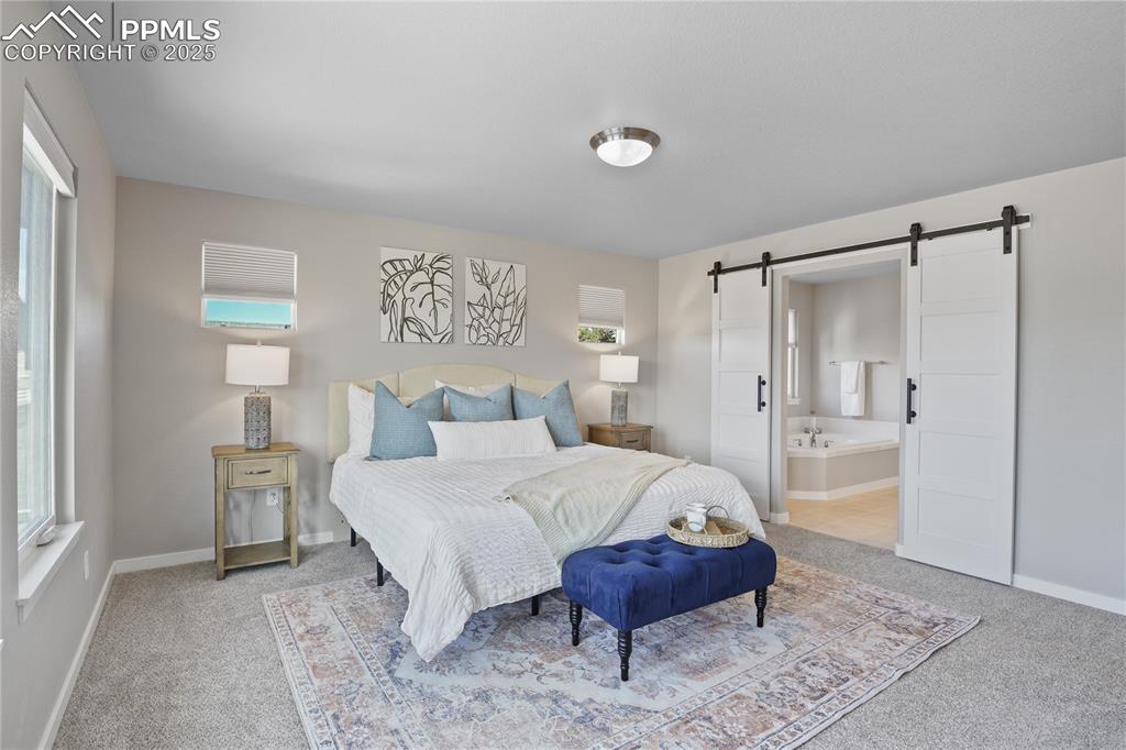 Image 30 of 50: Bedroom featuring a barn door, light carpet, and baseboards