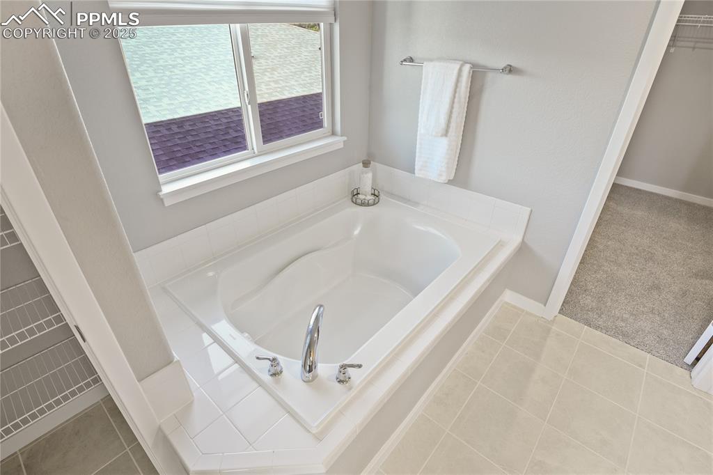 Image 33 of 50: Bathroom featuring a bath, baseboards, and a spacious closet