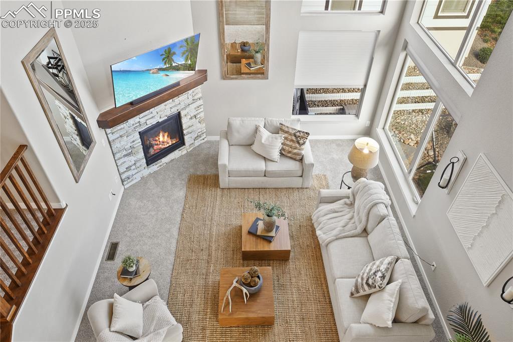 Image 35 of 50: Carpeted living room with a stone fireplace, stairs, a high ceiling, and ba
