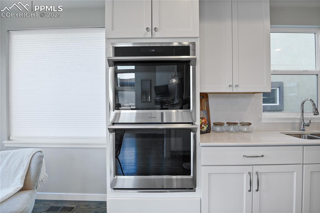 Image 8 of 50: Kitchen with double oven, a sink, white cabinetry, and tasteful backsplash