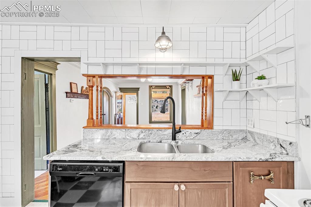 Image 28 of 50: Kitchen with black dishwasher, a sink, open shelves, light stone counters a