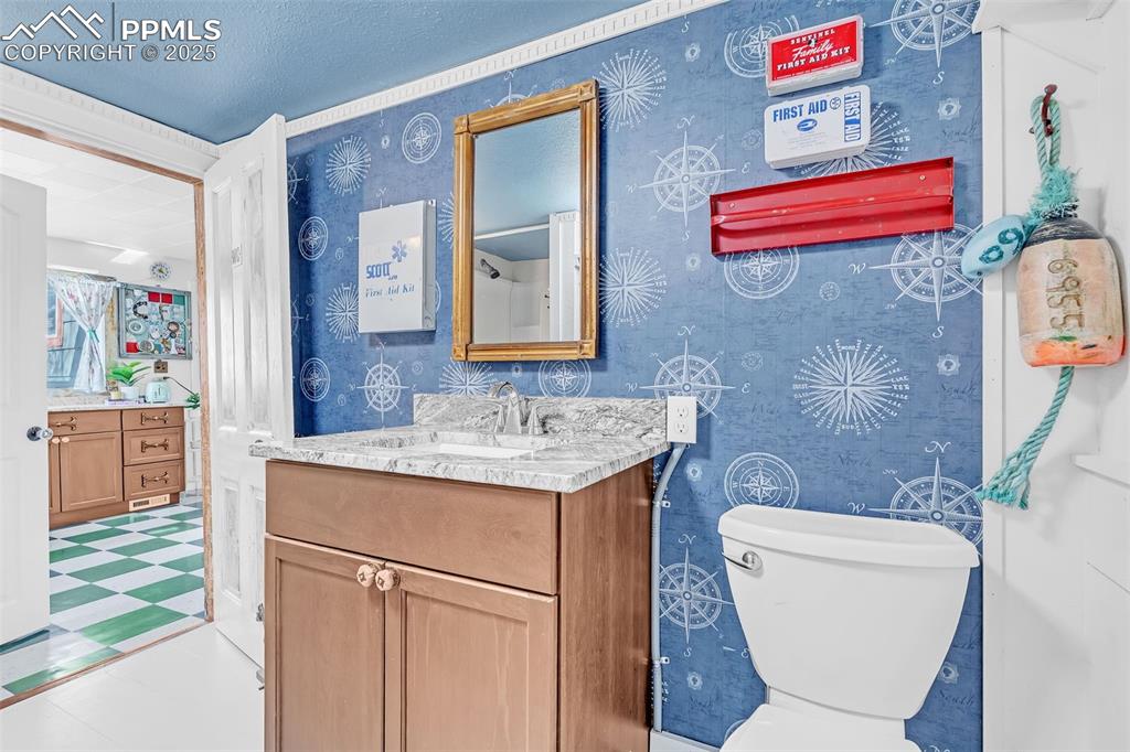 Image 39 of 50: Bathroom with tile patterned floors, toilet, vanity, wallpapered walls, and