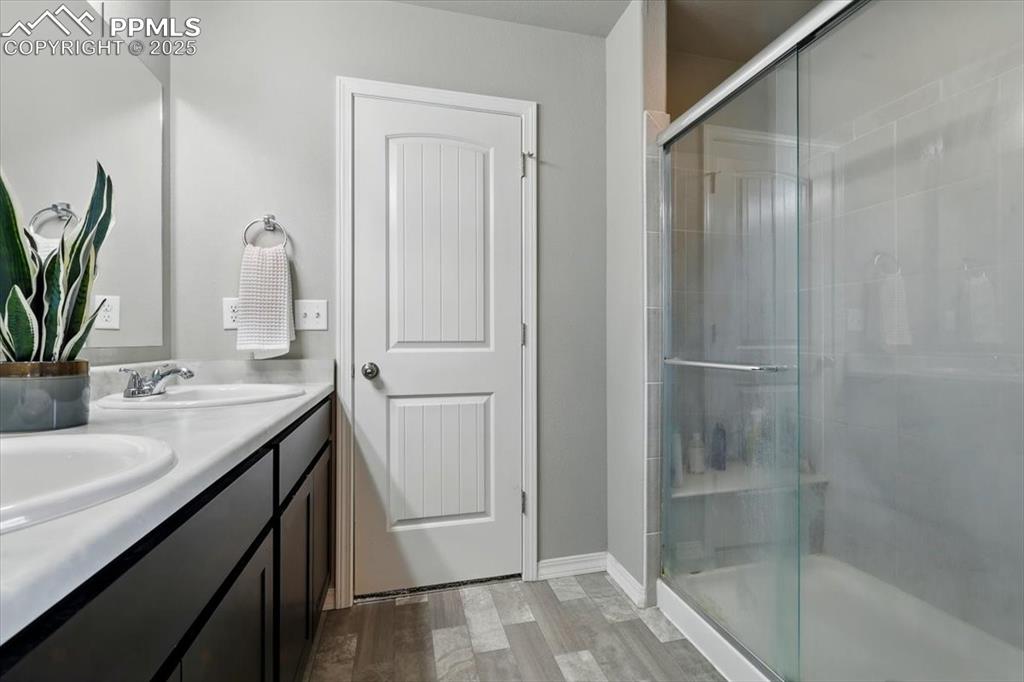 Image 28 of 45: Bathroom with double vanity, a shower stall, and wood finished floors