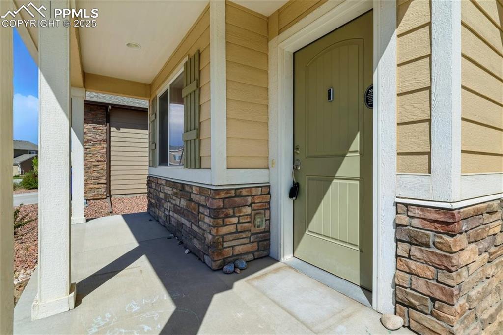 Image 3 of 45: Doorway to property with covered porch, stone siding, and brick siding