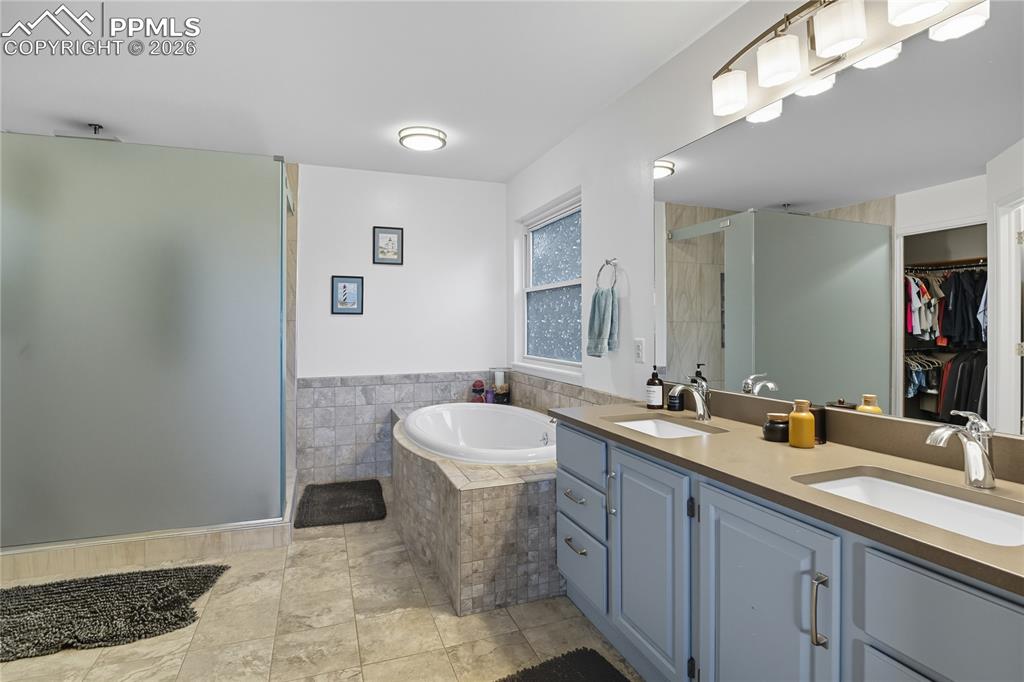 Image 27 of 45: Bathroom with double vanity, a bath, and a walk in closet