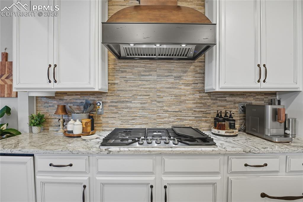 Image 7 of 45: Kitchen featuring range hood, white cabinets, light stone counters, and sta