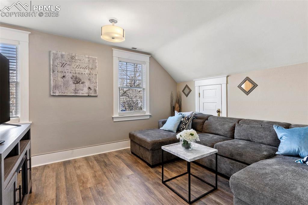 Image 18 of 43: Living area featuring dark wood-style floors, vaulted ceiling, and baseboar