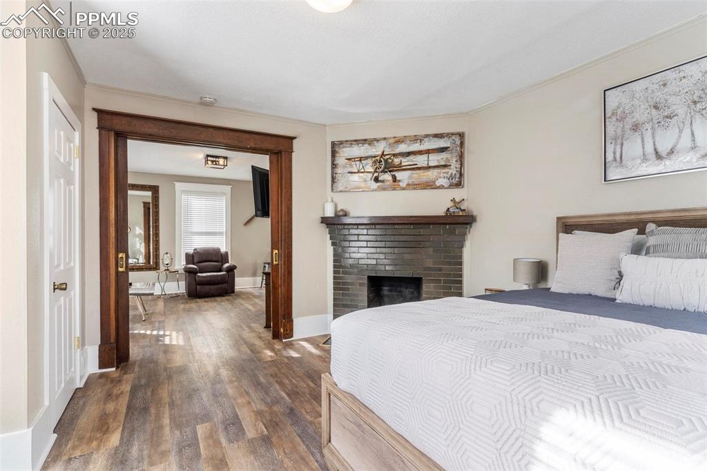 Image 5 of 43: Bedroom with dark wood-style flooring, a brick fireplace, crown molding, an