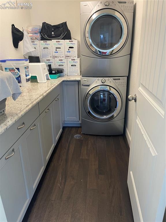 Image 15 of 25: Laundry area featuring stacked washer / drying machine, dark wood-style flo