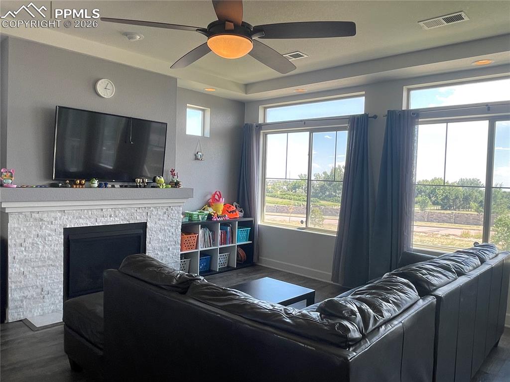 Image 5 of 25: Living area with dark wood-style flooring, a ceiling fan, a stone fireplace