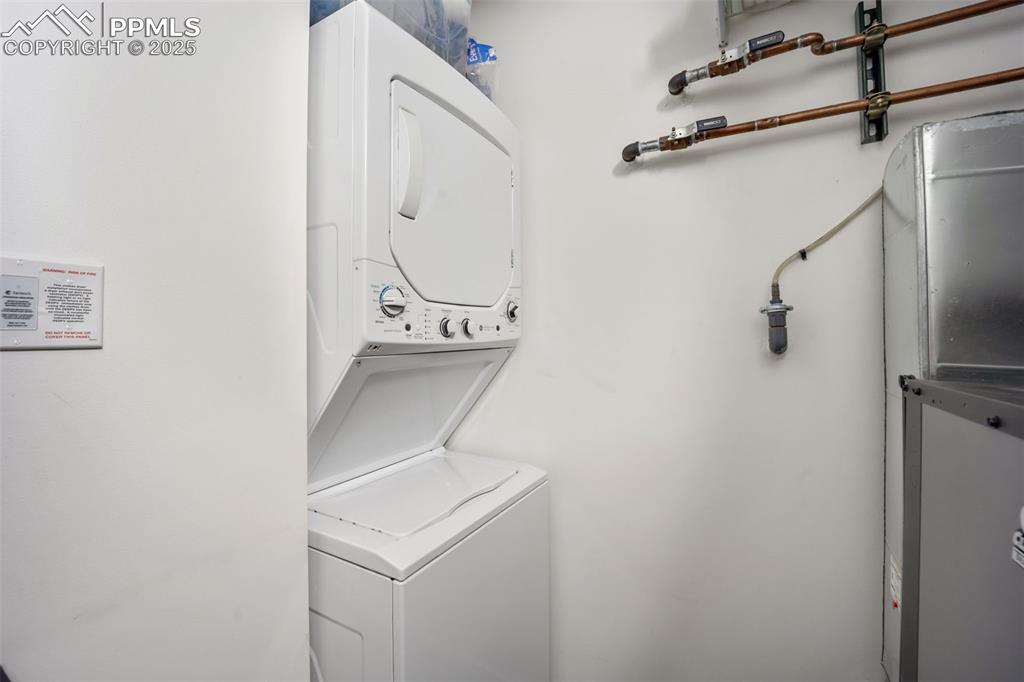 Image 43 of 50: Laundry area featuring estacked washer and dryer and heating unit