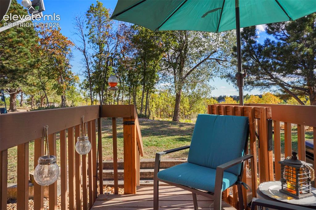 Image 15 of 28: Elevated wooden deck featuring a perimeter railing, mature trees, and a nat
