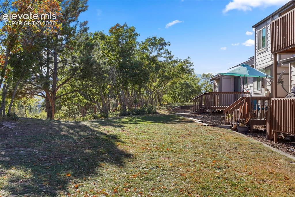 Image 23 of 28: Expansive lawn area, mature trees, multi-level wood deck, and wood-sided ex