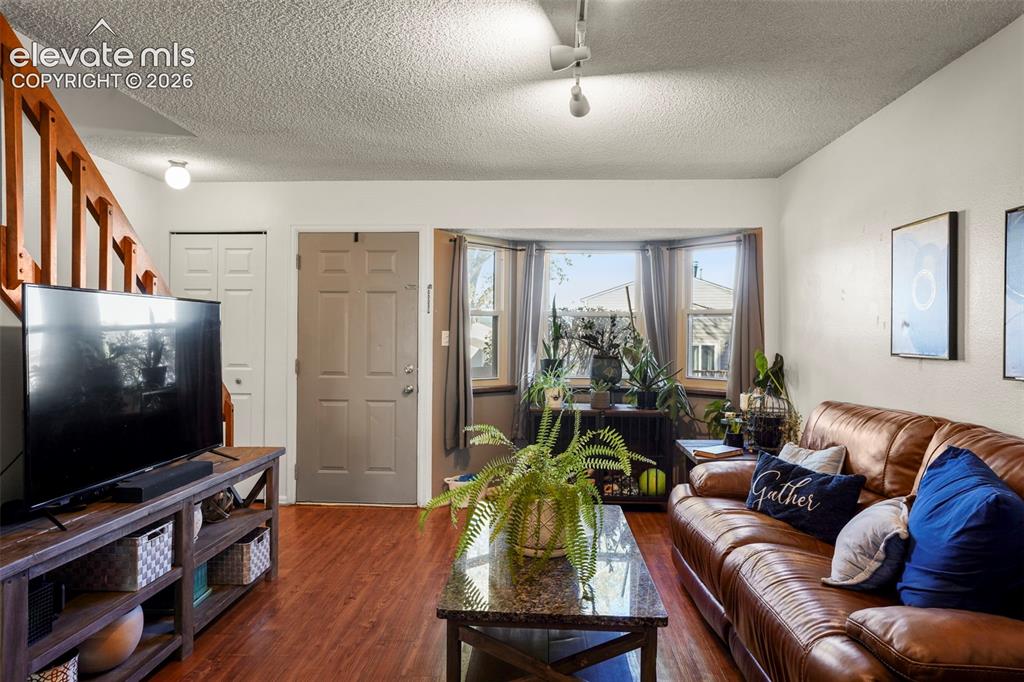 Image 4 of 28: Living area featuring wood-finish flooring, a bay window, a staircase with 
