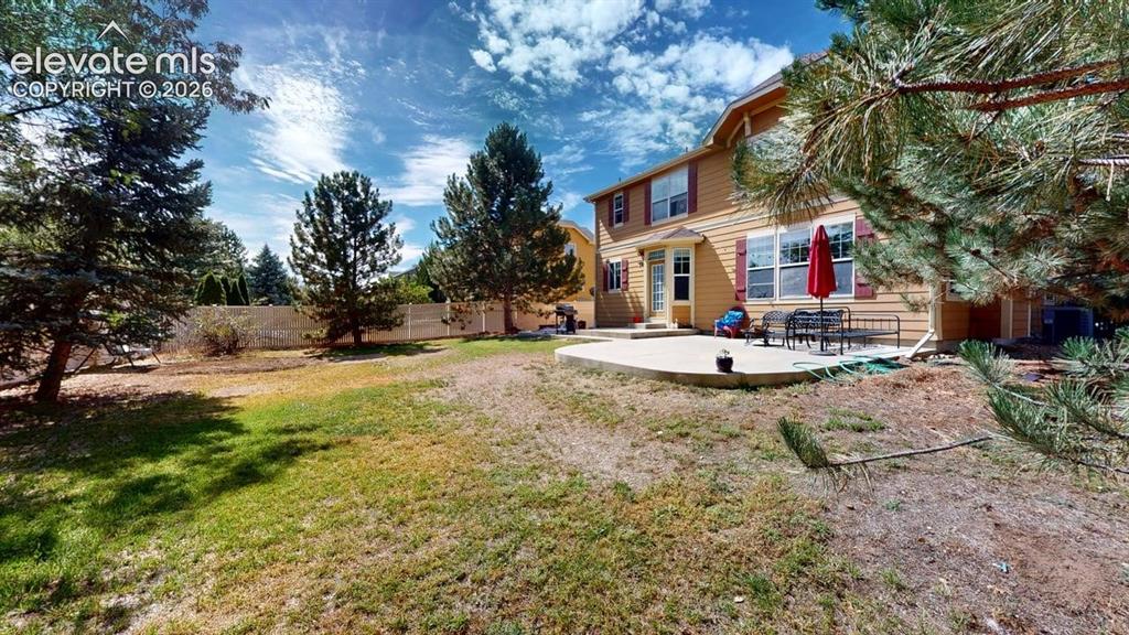 Image 3 of 22: Expansive backyard with a concrete patio, mature trees, and a privacy fence