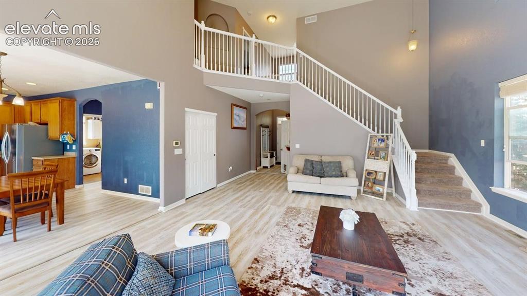 Image 9 of 22: Two-story great room with a staircase featuring white railings and carpeted