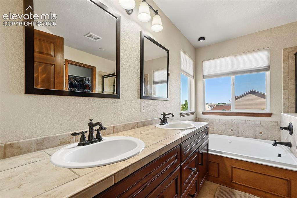 Image 8 of 34: Dual vanity with dark wood-finish cabinetry, tile countertop, and matching