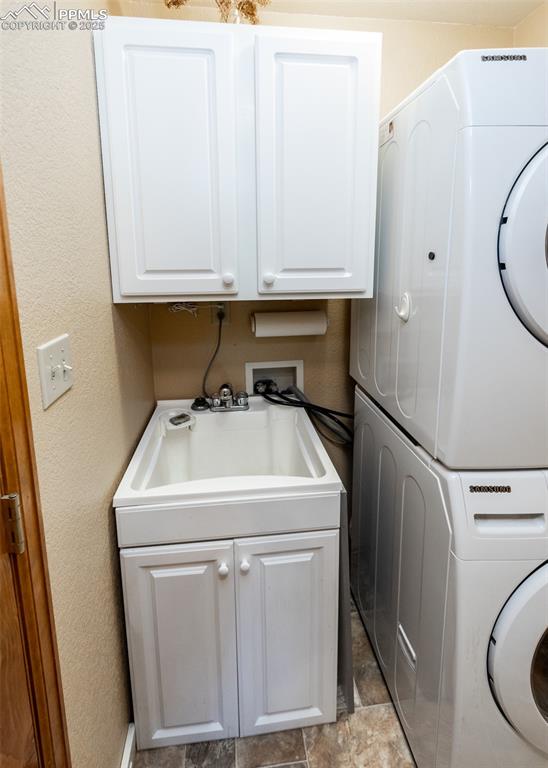 Image 23 of 48: Stack washer and dryer and convenient laundry sink and cabinets.