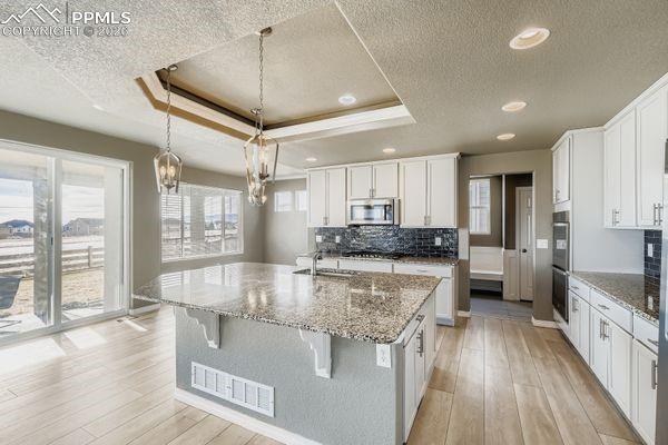 Image 12 of 35: Kitchen featuring white cabinetry, light stone counters, light wood-style f
