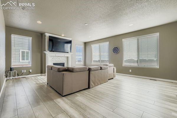 Image 15 of 35: Living room featuring a fireplace, light wood-type flooring, a textured cei