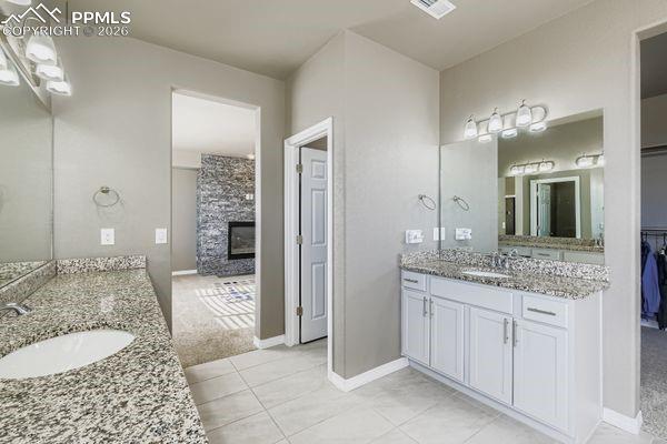 Image 24 of 35: Bathroom with a fireplace, two vanities, a spacious closet, light tile patt