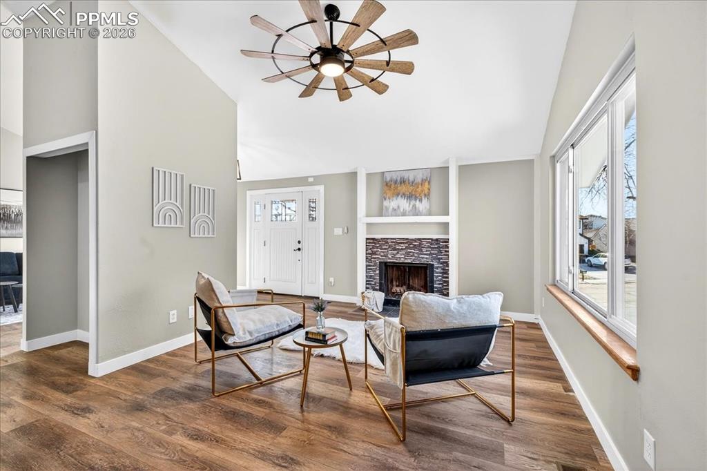 Image 12 of 49: Living room with a fireplace, wood finished floors, a ceiling fan, healthy
