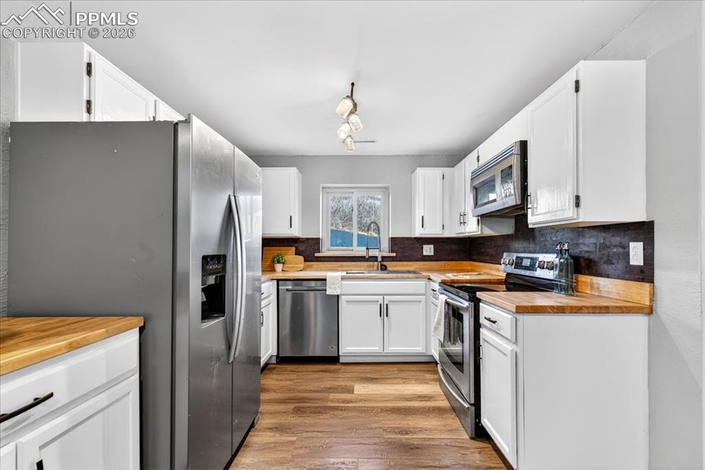 Image 19 of 49: Kitchen with butcher block counters, stainless steel appliances, white cabi
