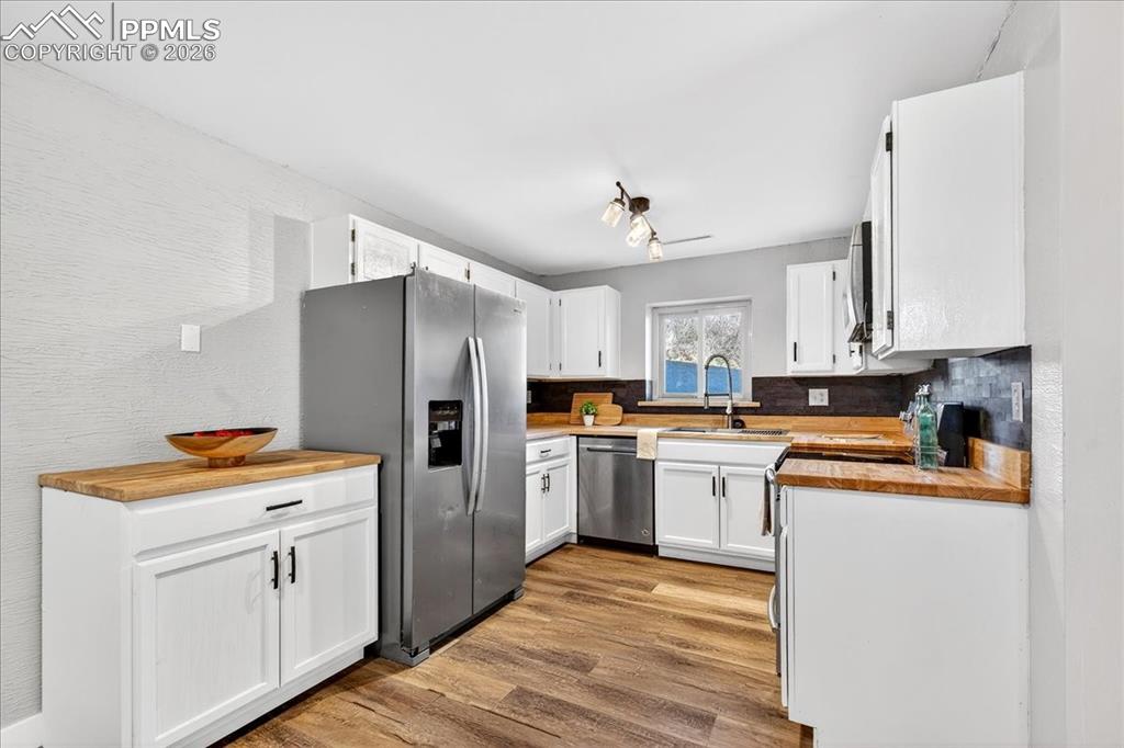 Image 20 of 49: Kitchen with stainless steel appliances, wood counters, white cabinetry, li