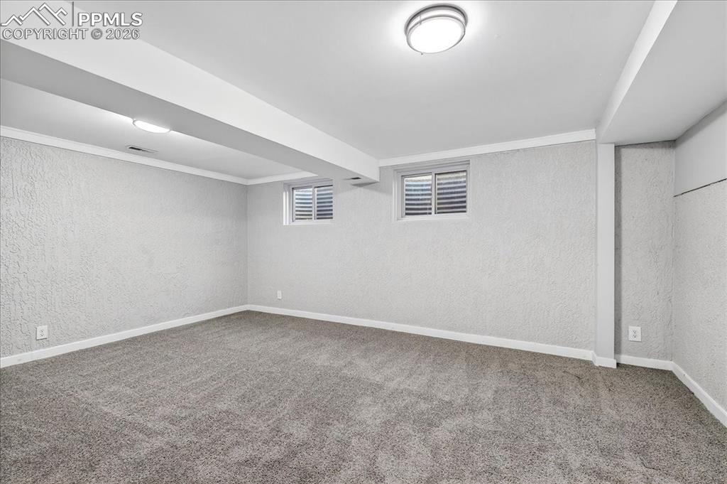 Image 32 of 49: Below grade area with a textured wall, carpet flooring, and ornamental mold