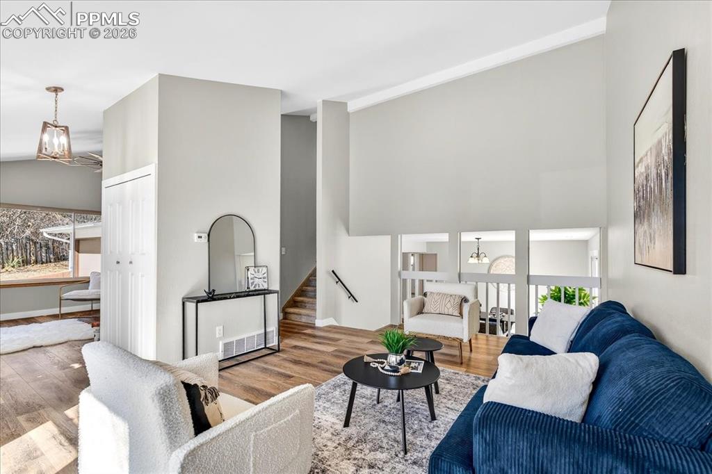 Image 8 of 49: Living room with hanging lights, wood finished floors, and a high ceiling