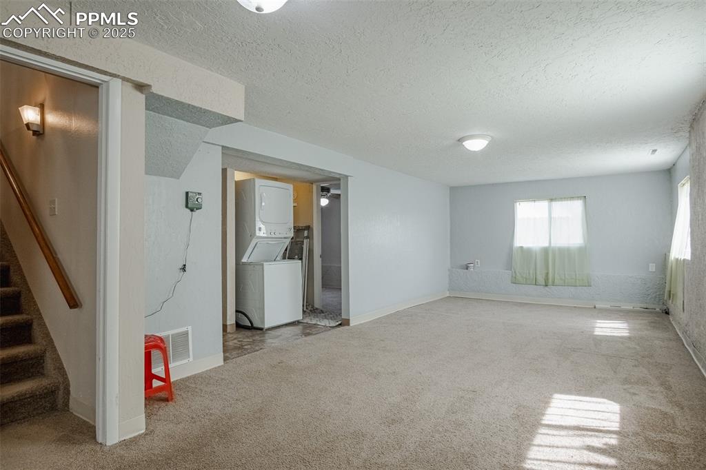 Image 34 of 44: Below grade area featuring visible vents, stacked washer / dryer, a texture