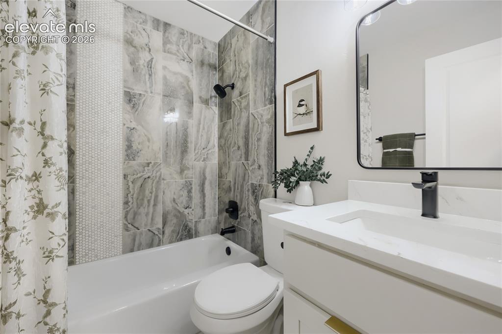 Image 18 of 42: Bathtub with a shower featuring large format tile and a mosaic accent strip