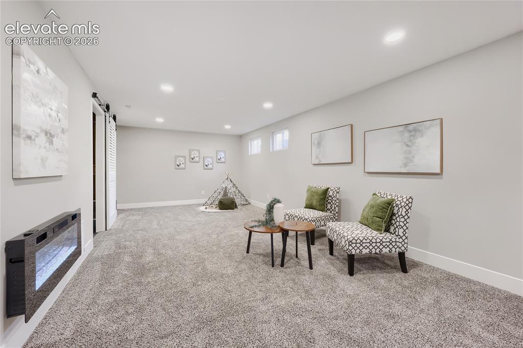 Image 25 of 42: Wall-mounted electric fireplace, recessed lighting, gray carpeting, dual sl