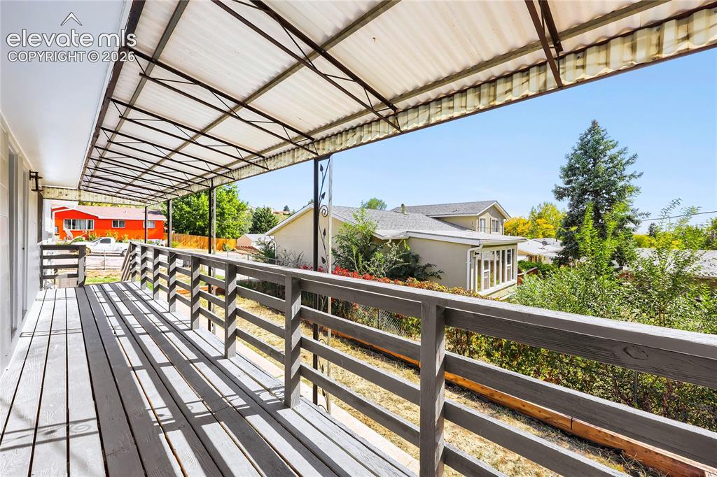 Image 34 of 42: Covered outdoor deck with wood-finish flooring and slatted railing
