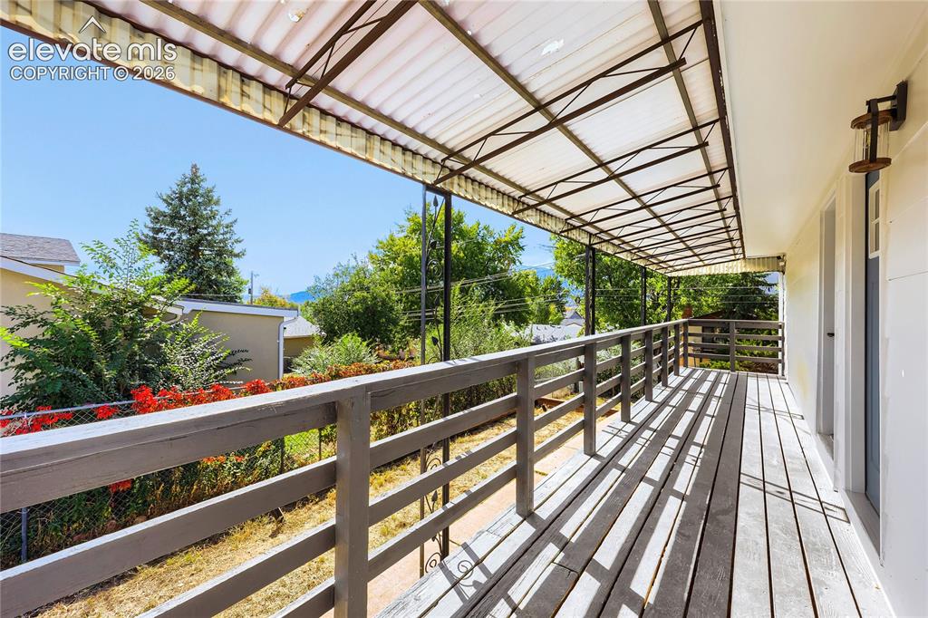 Image 35 of 42: Covered outdoor deck with wood railing, wood-finish flooring, and wall-moun