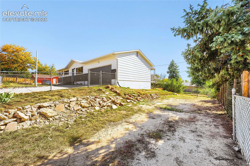Image 36 of 42: White siding exterior with an attached garage, chain-link fencing, and a re