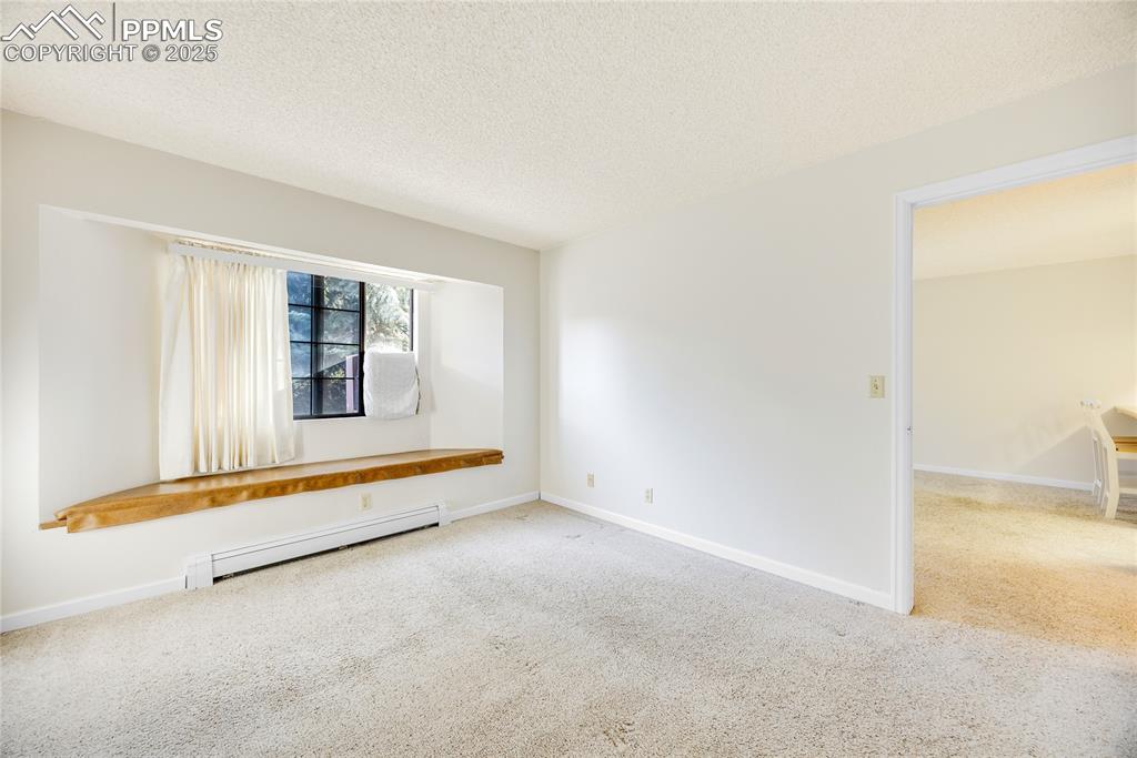 Image 11 of 17: Unfurnished room with carpet floors, a baseboard radiator, and a textured c