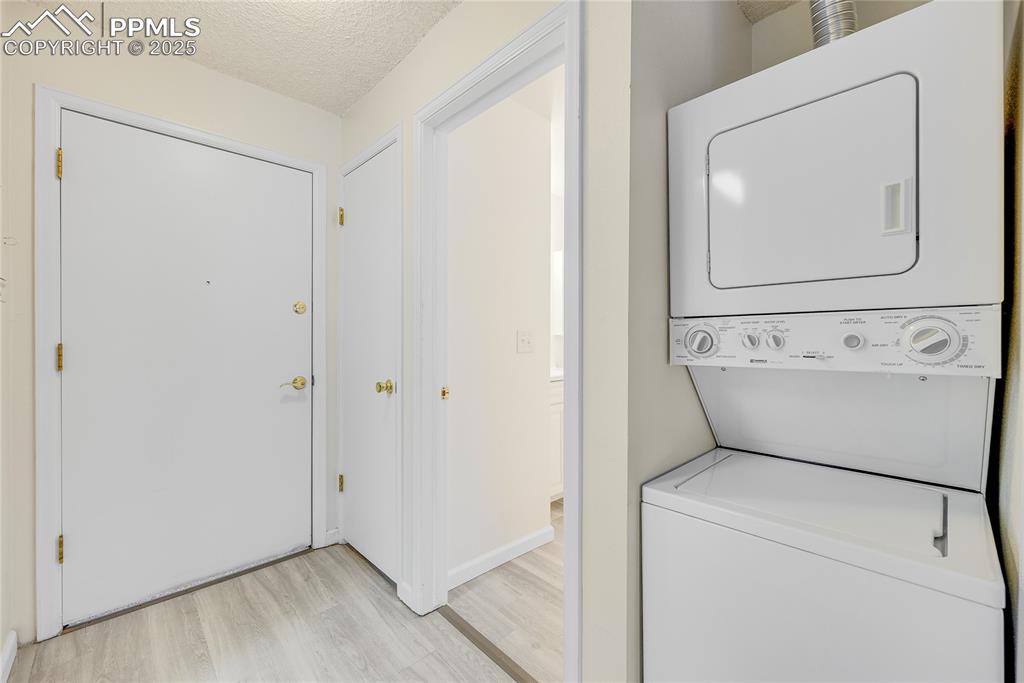 Image 14 of 17: Laundry area with a textured ceiling, stacked washer / dryer, and light woo