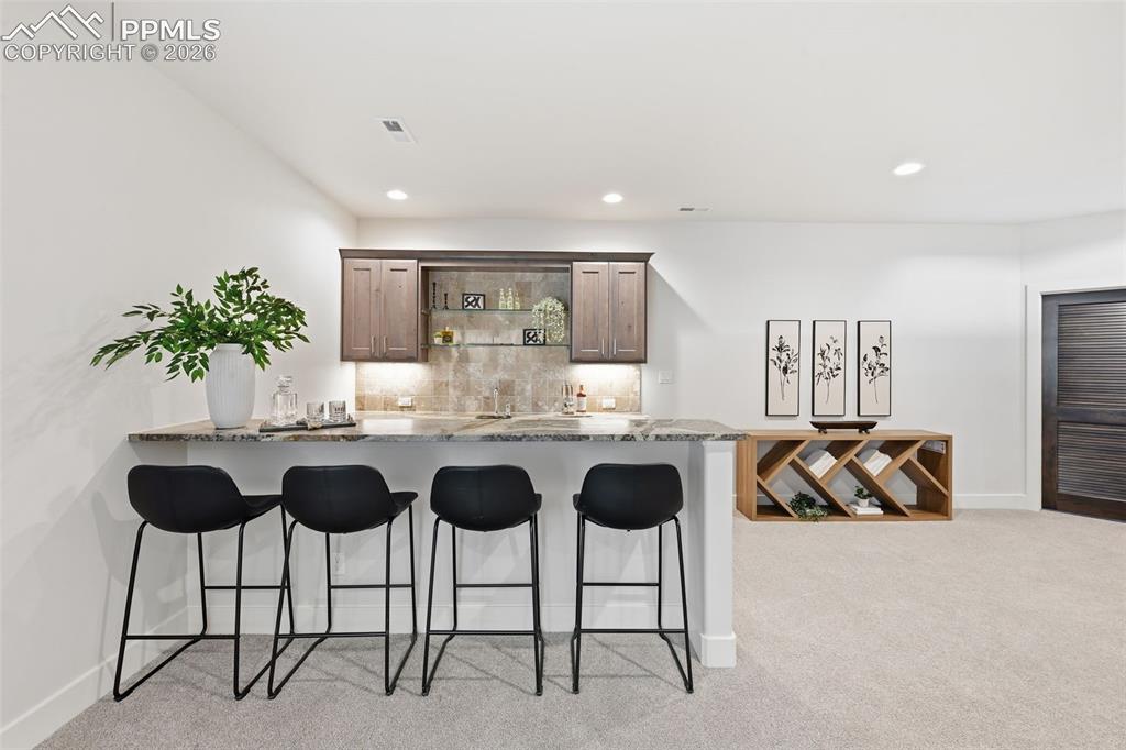 Image 26 of 39: Wet bar featuring a polished stone countertop, wood cabinetry, and recessed
