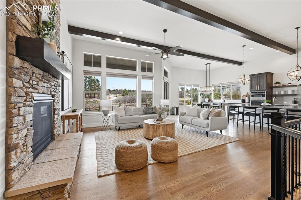 Image 7 of 39: Spacious living area featuring a stone-clad fireplace with hearth, high cei