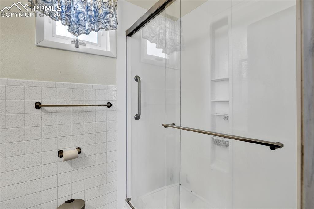 Image 17 of 49: Bathroom featuring vanity, a shower, crown molding, and tile walls