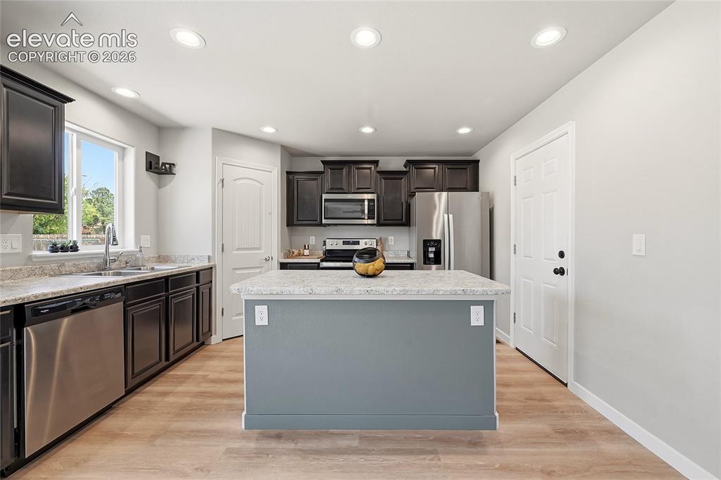 Image 10 of 30: Kitchen featuring a central island with a light-toned countertop, dark wood